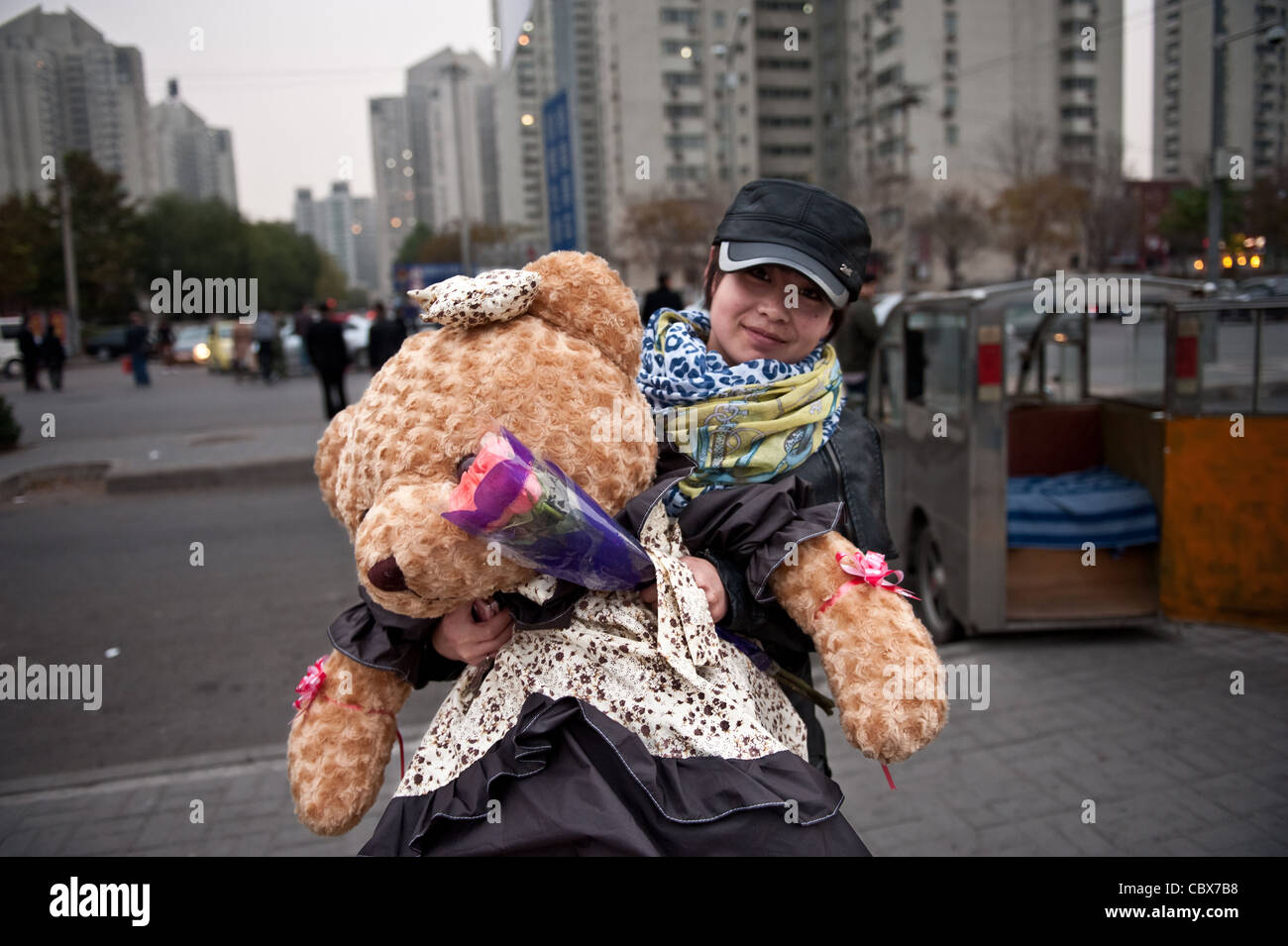 Beijing, Wangjing. A young woman on her way to a friend with a teddy bear and flowers as  presents. Stock Photo