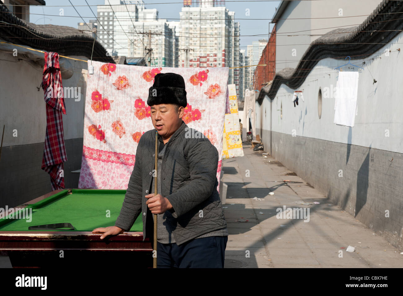 Xiadian, Beijing. Man playing pool in a poor neighborhood with in the background Beijing's Central Business District. Stock Photo