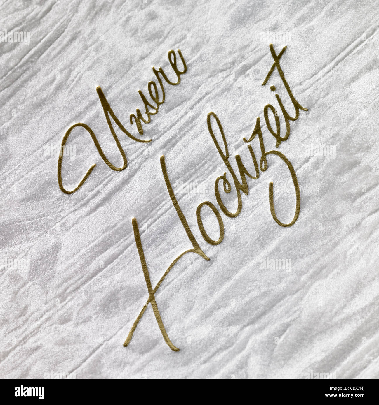 'Unsere Hochzeit' written in golden engraved Letters on abstract grey back Stock Photo