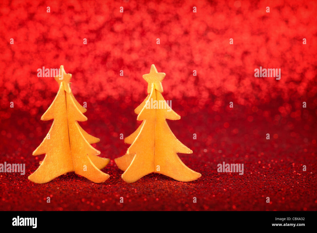 Two golden paper Christmas trees with stars on tops, over red glitter ...