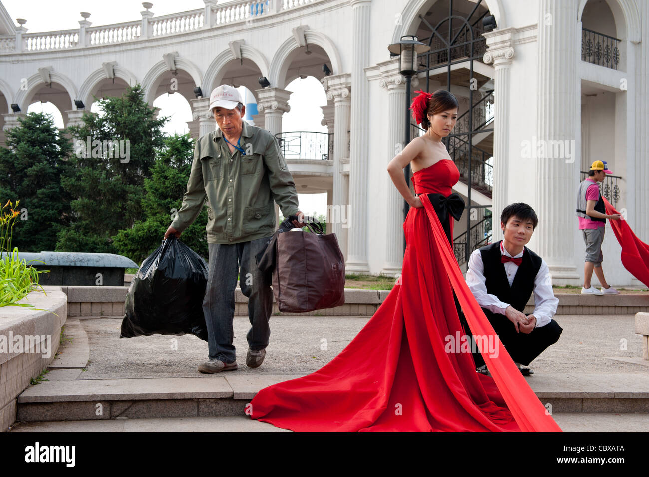 Beijing, Chaoyang Park. Worker carrying garbage passing a wedding photo shoot. Stock Photo