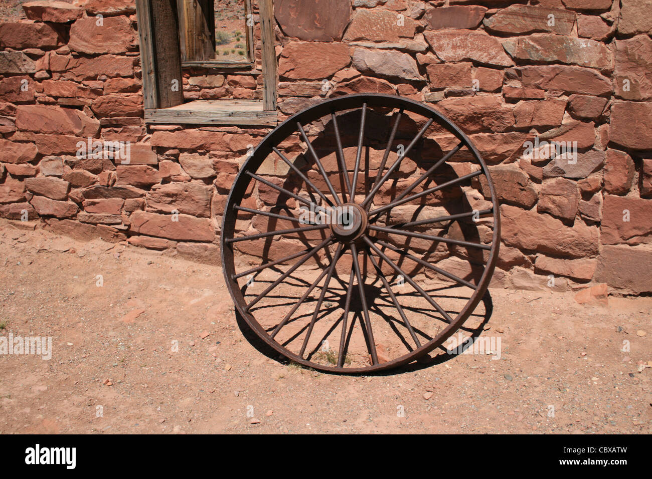 antique iron wheel leans against a stone wall at Lees Ferry , Arizona Stock Photo