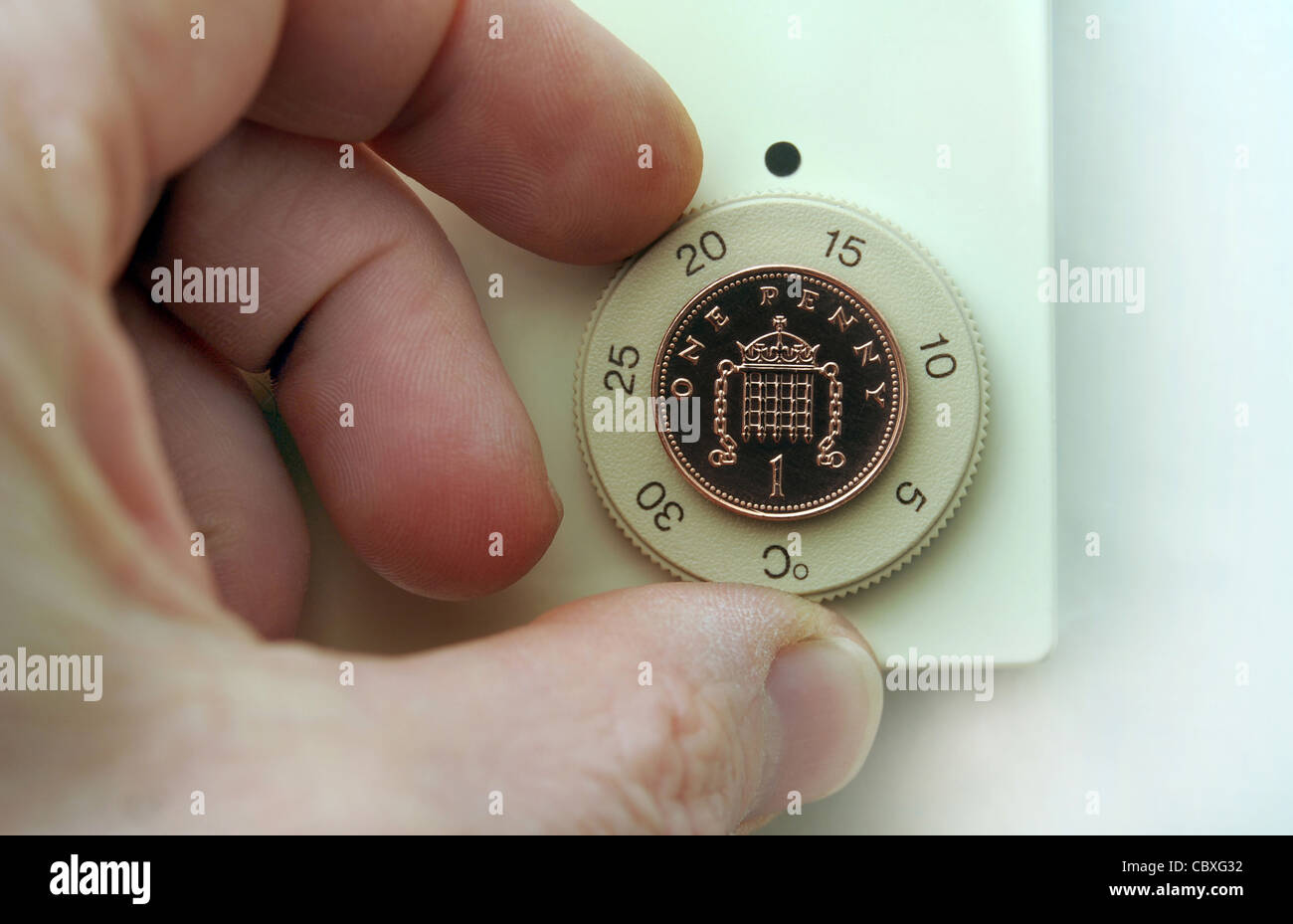 BRITISH THERMOSTAT BEING TURNED BY MANS HAND WITH PENNY IN CENTRE RE HEATING COSTS  HOMES REDUCING CENTRAL HEATING FUEL UK Stock Photo
