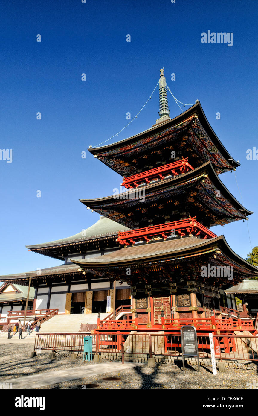 NARITA, Japan - The Three Storied Pagoda, standing 25 meters tall, was originally built in 1712. It is ornately decorated with brightly painted rafters, carved dragons, and sculptures of 16 RAKAN or Buddha's disciples how attained Nirvana. On the first floor's inner sanctum is GOCHI-NYORAI (Five Tathagas) who is believed to be endowed with the five wisdoms of Buddha. In the background is the front of the Great Main Hall. The Narita-san temple, also known as Shinsho-Ji (New Victory Temple), is Shingon Buddhist temple complex, was first established 940 in the Japanese city of Narita, east of Tok Stock Photo