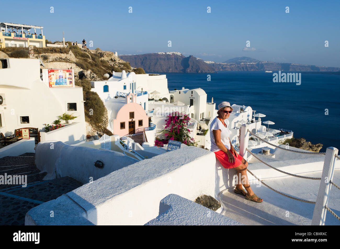 Santorini, Oia, Cyclades Islands, Greece, view with an elderly woman sitting on stoop, overlooking the ocean Stock Photo