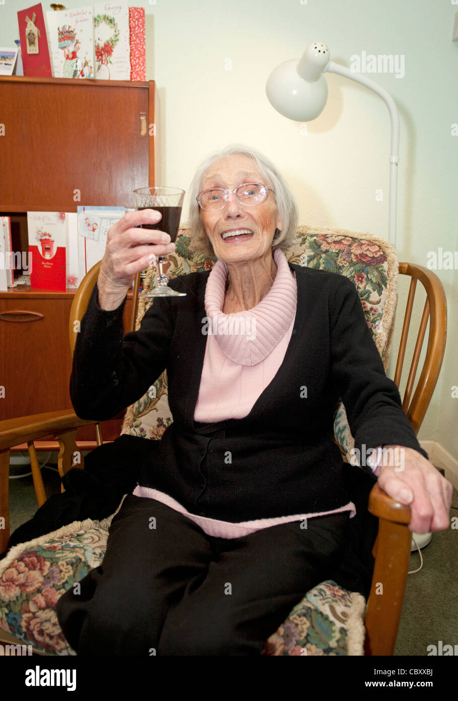 old age pensioner sat in chair celebrating with a glass of port Stock Photo