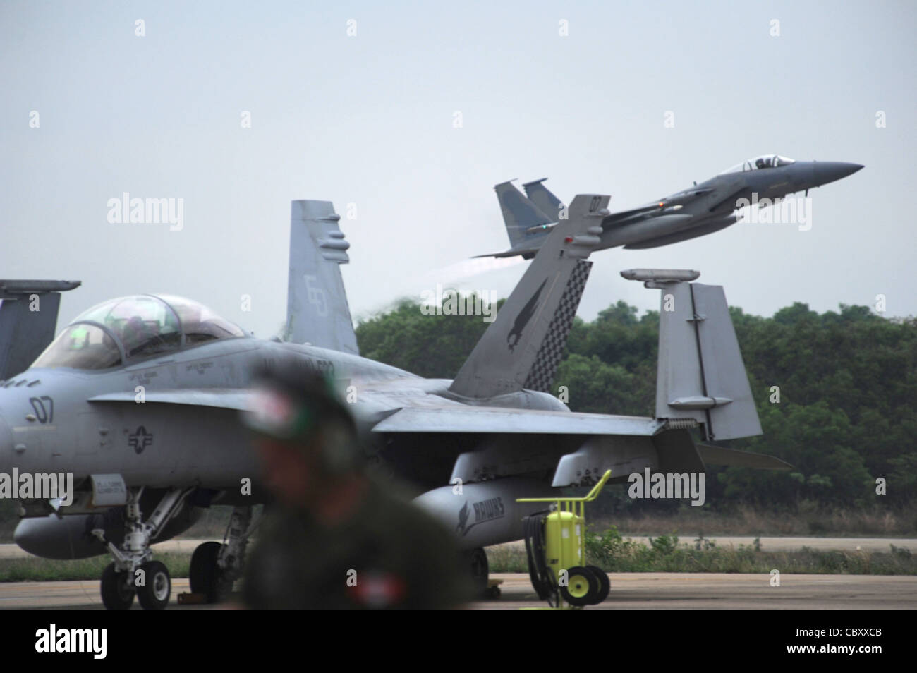 An F-15 Eagle assigned to the 44th Expeditionary Fighter Squadron at Kadena Air Base, Japan, takes off March 23, 2011, from Korat Royal Air Force Base, Thailand, behind a parked F/A-18 Hornet assigned to Marine All-Weather Fighter Attack Squadron 533 at Marine Corps Air Station Iwakuni, Japan. The Eagle was flying an exercise mission that was part of Cope Tiger 2011, which runs from March 14 through 25. Participants of Cope Tiger include the U.S. Air Force, the U.S. Marine Corps, the Royal Thai Air Force, Royal Thai Army and the Republic of Singapore Air Force. Stock Photo