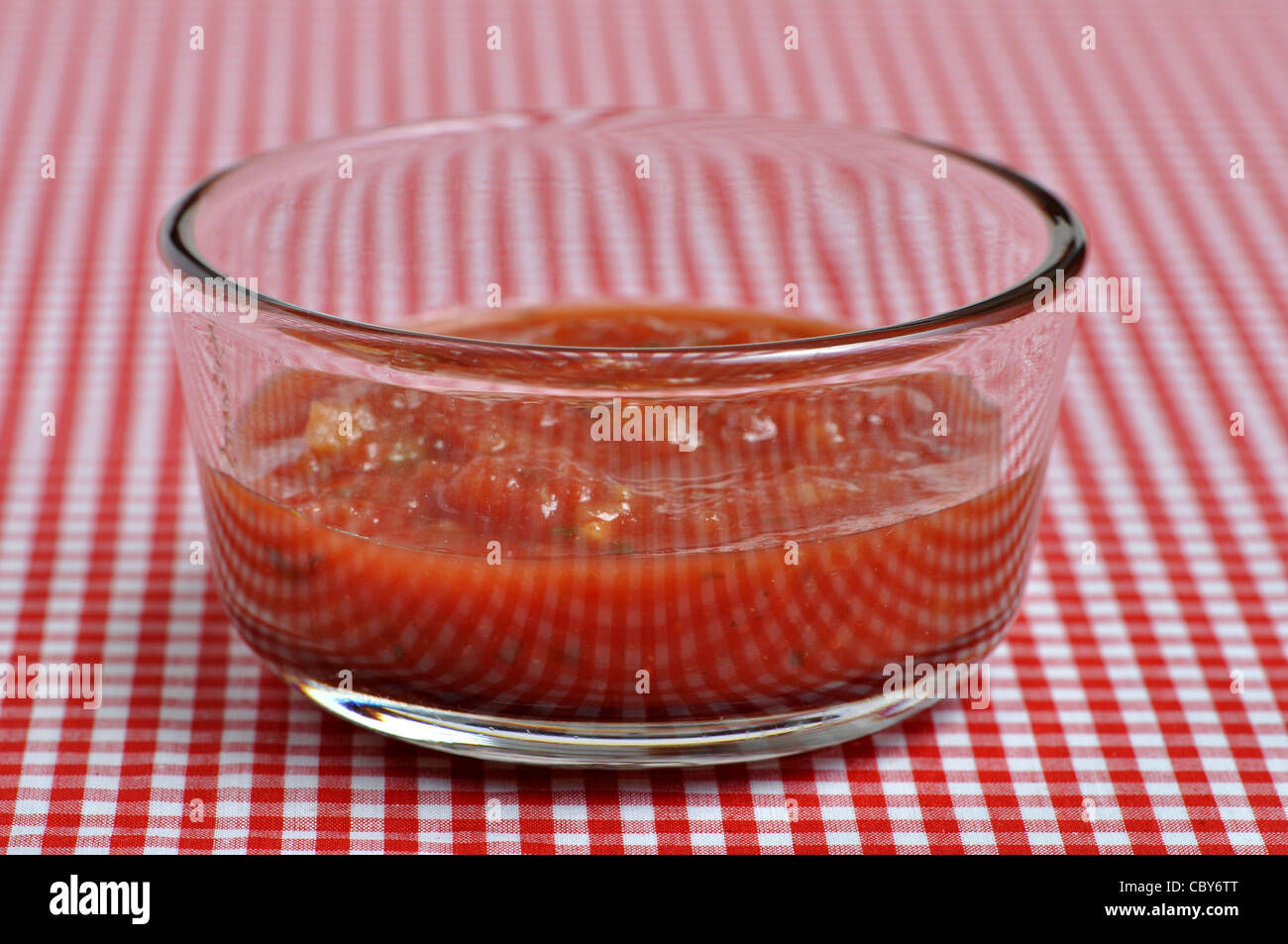 A small dish of salsa sits on a red and white checker table cloth. Stock Photo