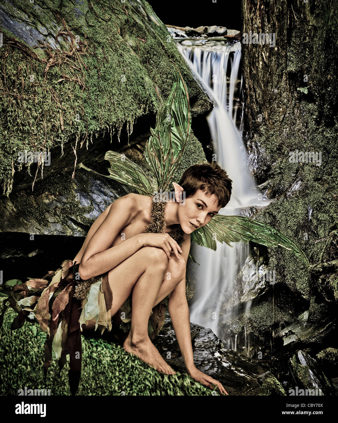 Faerie (pixie) on moss covered rock near small waterfall. Stock Photo