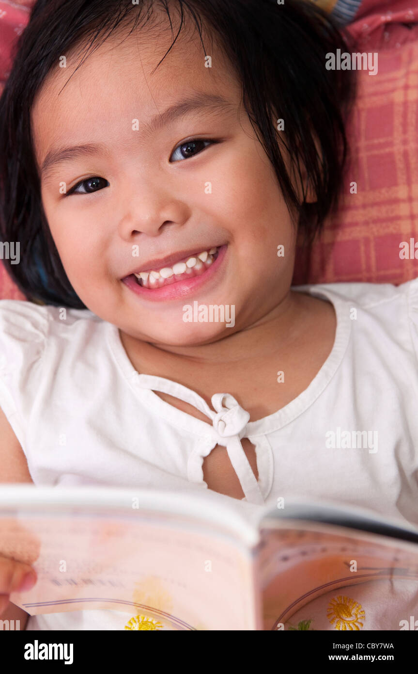 Little Asian girl lying on bed and reading Stock Photo Alamy