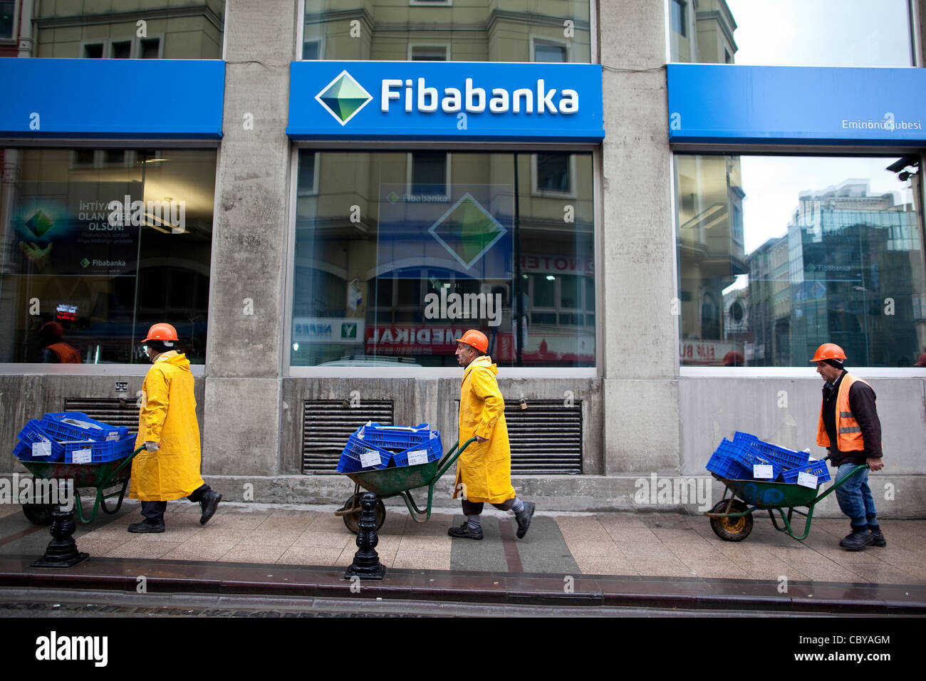 Workmen pushing wheelbarrows pass the private bank Fibabanka in central Istanbul, Turkey. Photo:Jeff Gilbert Stock Photo