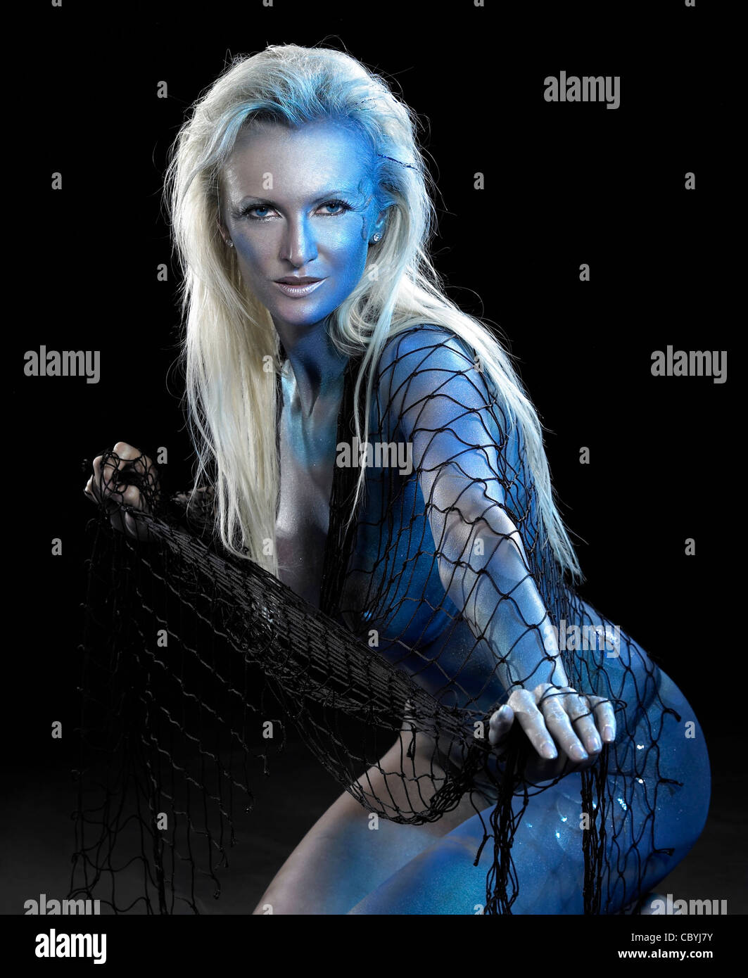 mystic mermaid theme showing a blue bodypainted woman posing with net in black back Stock Photo