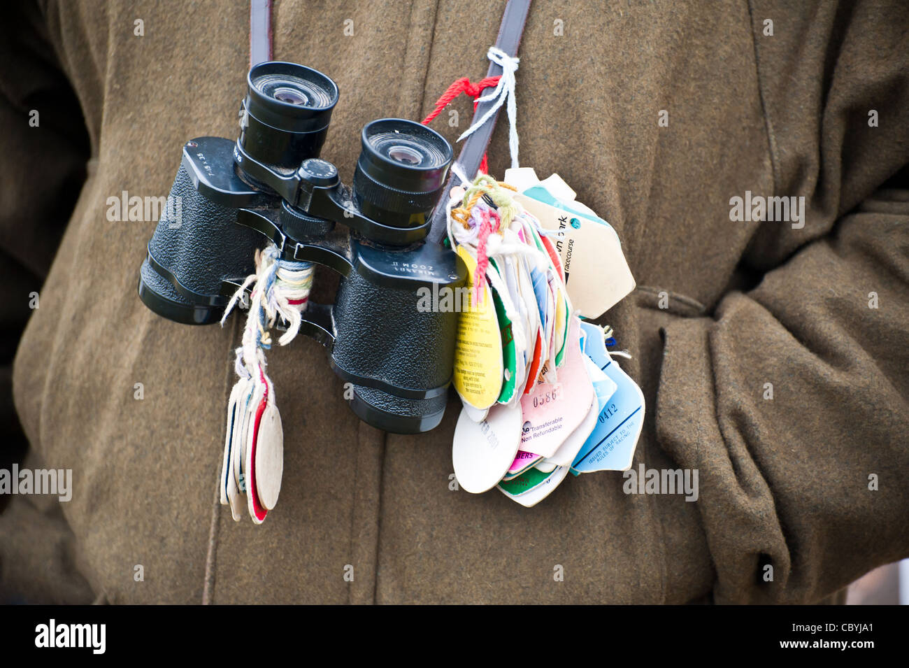 Pair of binoculars round a persons neck with lots of racecourse entry passes attached. Stock Photo