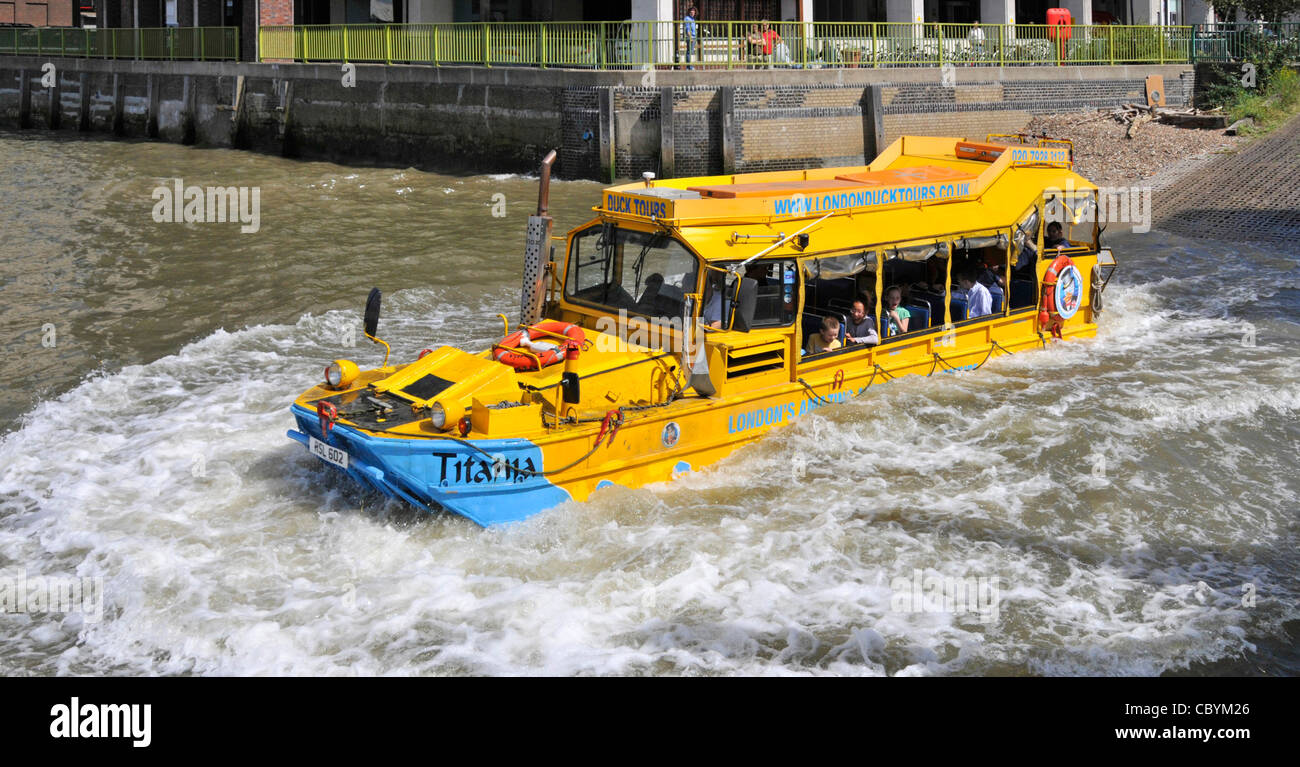 London UK business amphibious Duck Tours makes water splash entry into River Thames for tourist people to travel on sightseeing tour in yellow boat Stock Photo