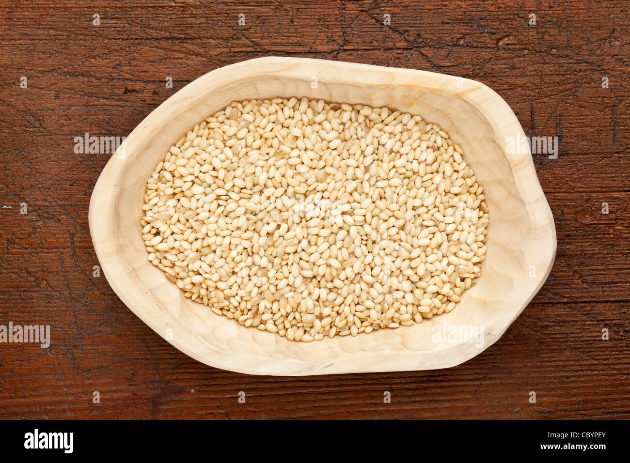 sweet brown rice grain in a rustic wood bowl against grunge dark wooden table surface, top view Stock Photo
