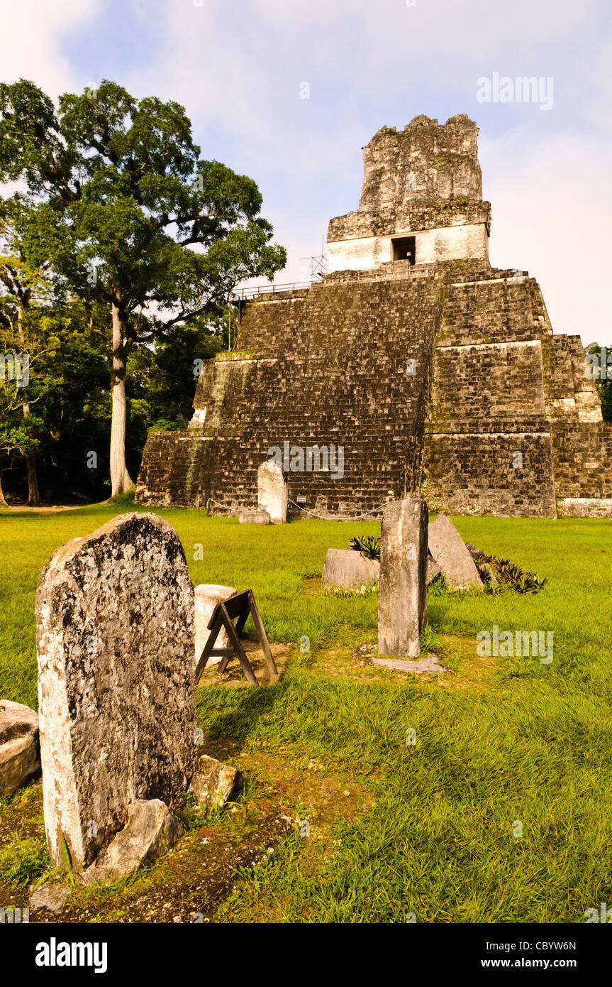 TIKAL, Guatemala - The Temple of the Masks, or Temple 2, in the Tikal Maya ruins in northern Guatemala, now enclosed in the Tikal National Park. In the foreground is a series of stela on the Main Plaza that once held commemorative inscriptions but that have since worn away over time. Visitors can climb wooden steps at the left of the pyramid to near the top. The section at the very top of the pyramid was once decorated in giant carved masks, only parts of which are still visible, and the entire pyramid would have been painted in bright colors. Stock Photo
