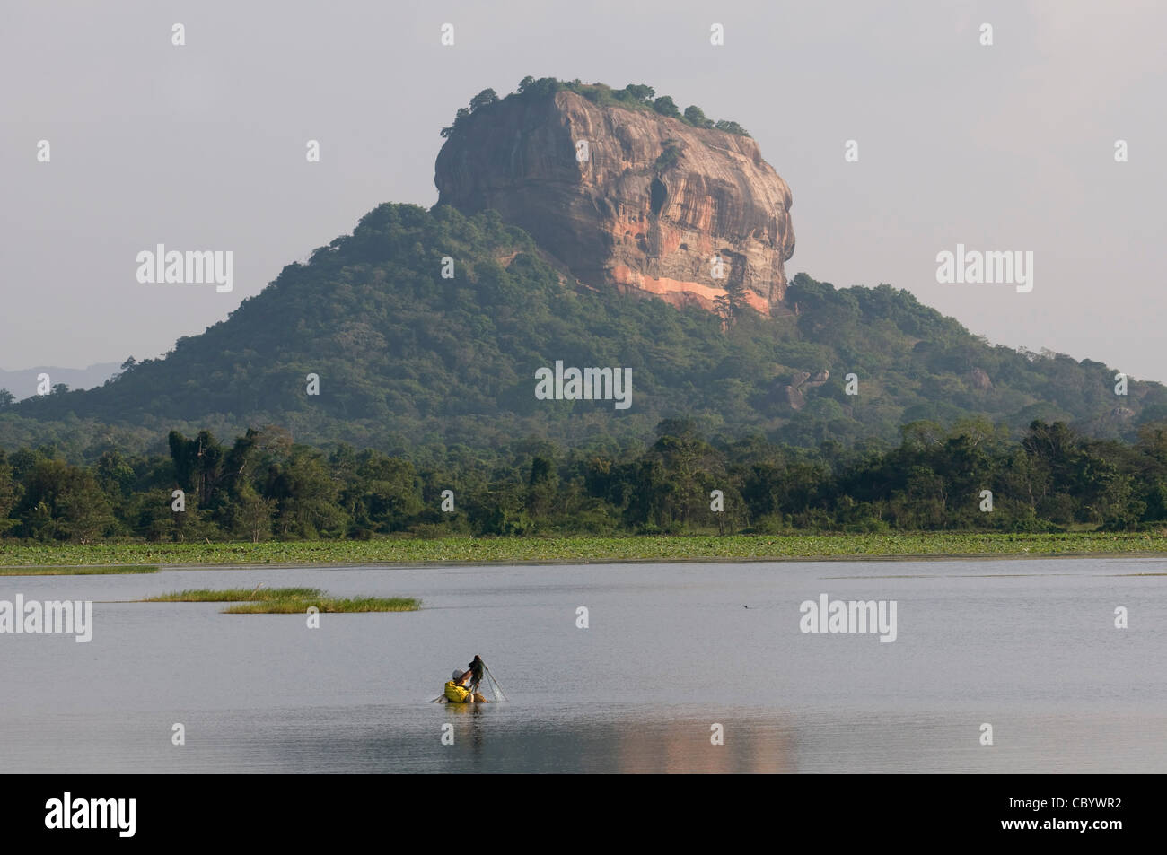 Sigiriya (Lion's rock), Sri Lanka seen cross a tank with a local fisher in the water. Stock Photo