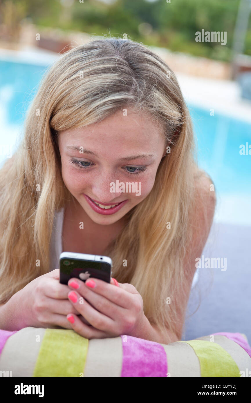 Attractive smiling 13 years old teenage girl in poolside holiday environment using her Apple