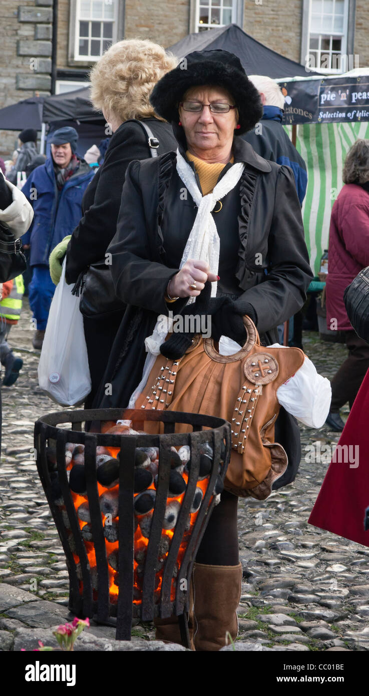 A Christmas shopper warming hands near a brazier during the Grassington Dickensian Christmas Festival Stock Photo