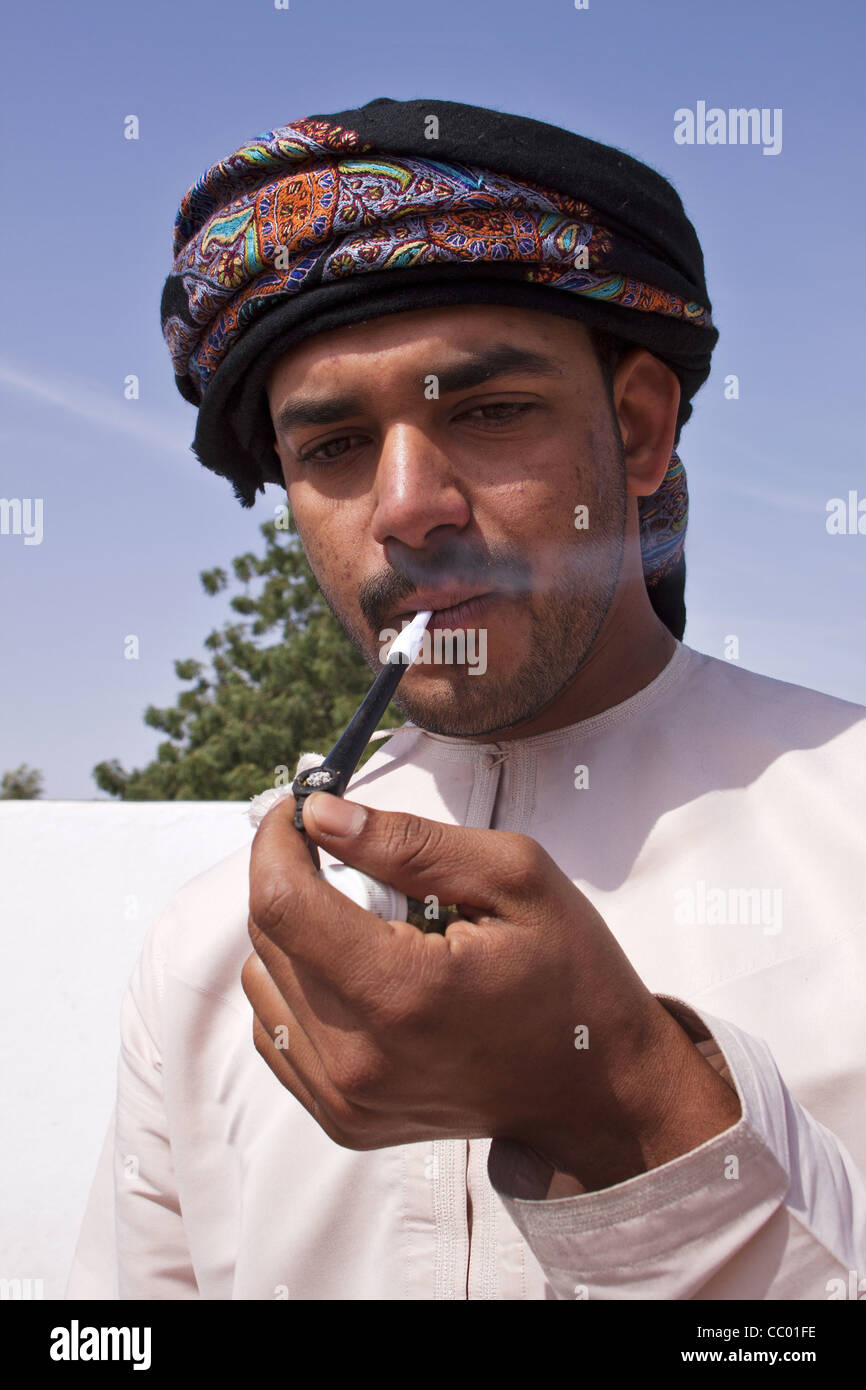 MAN IN THE TRADITIONAL DRESS (DISHDASHA) SMOKING AN OMANI PIPE, ROAD TO