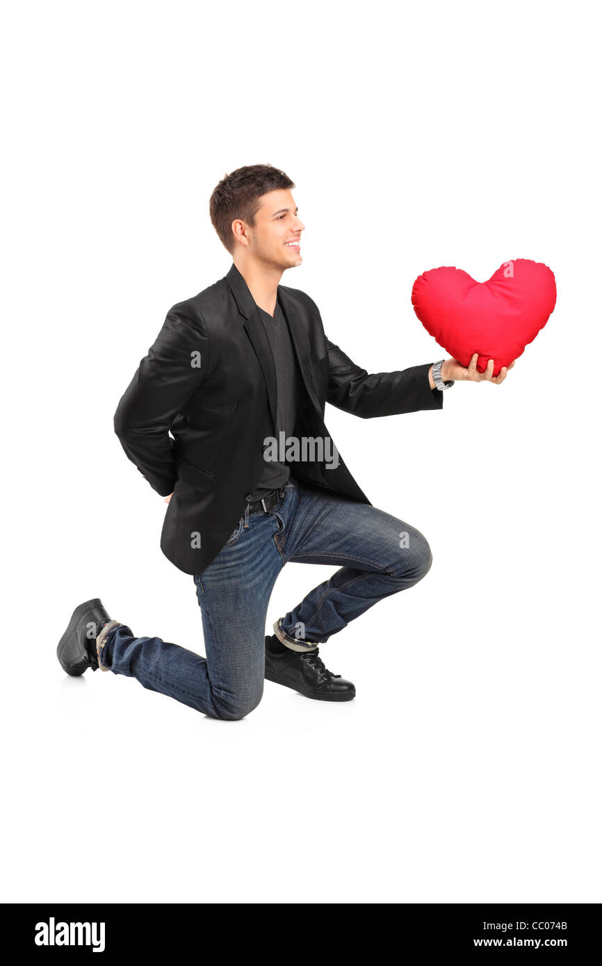 A romantic man on his knees practicing a proposal and holding a red heart shaped pillow Stock Photo