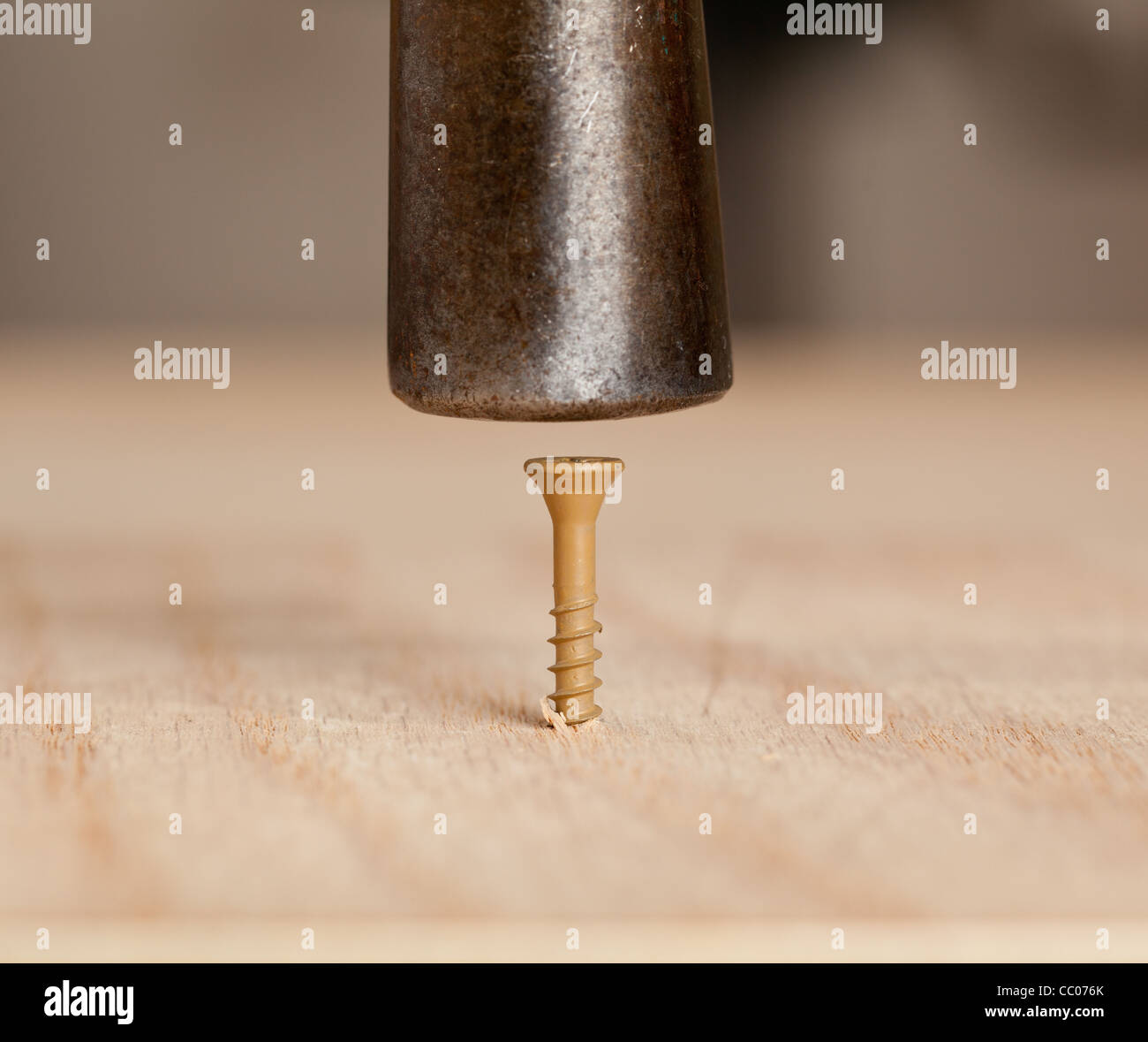 Brown screw being driven into wood by hammer head Stock Photo