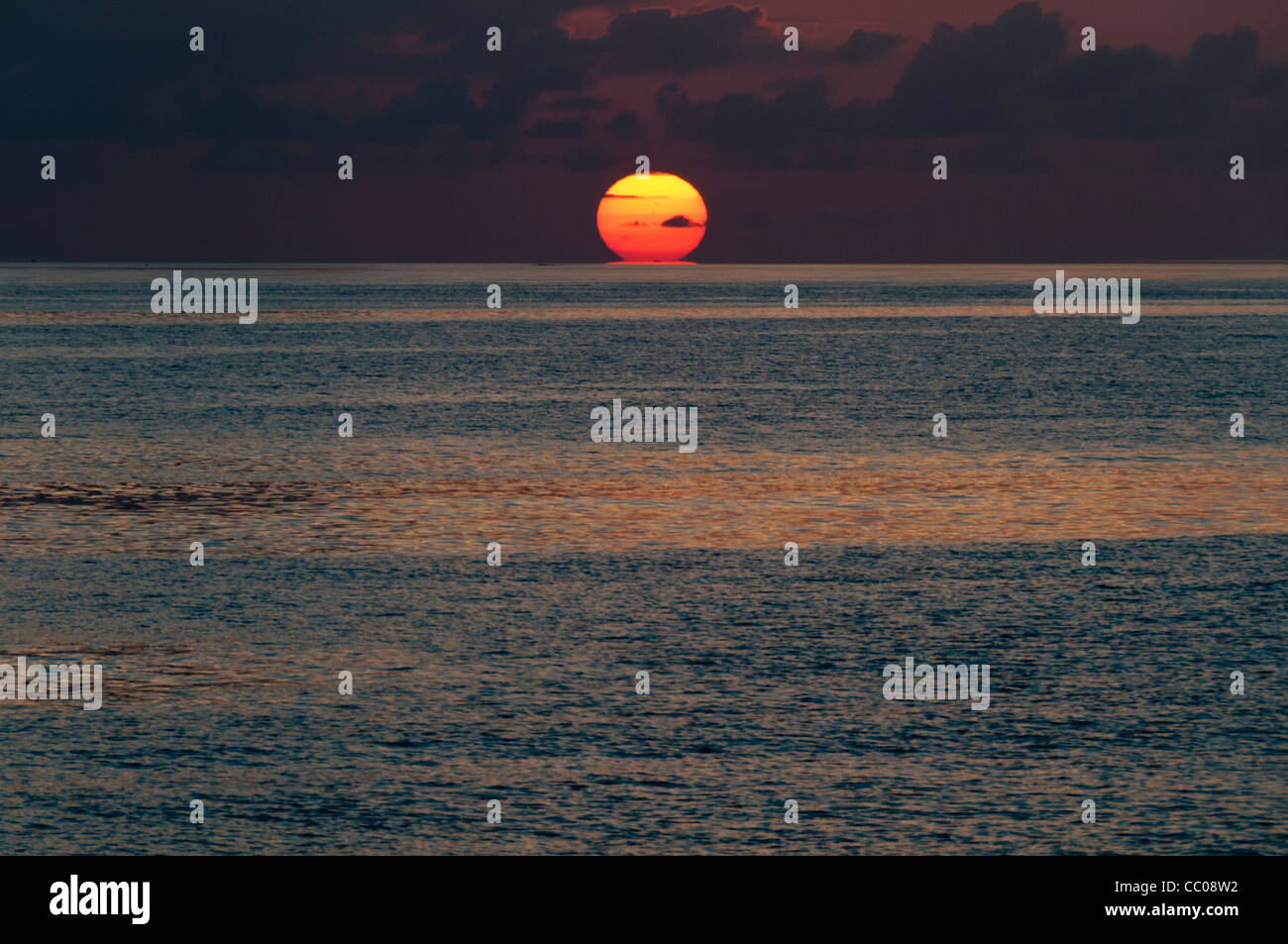 The sun first touches the horizon, with the calm waters of the Coral Sea in the foreground. Taken at Swains Reef on the southern end of the Great Barrier Reef of the coast of Queensland, Australia. Stock Photo