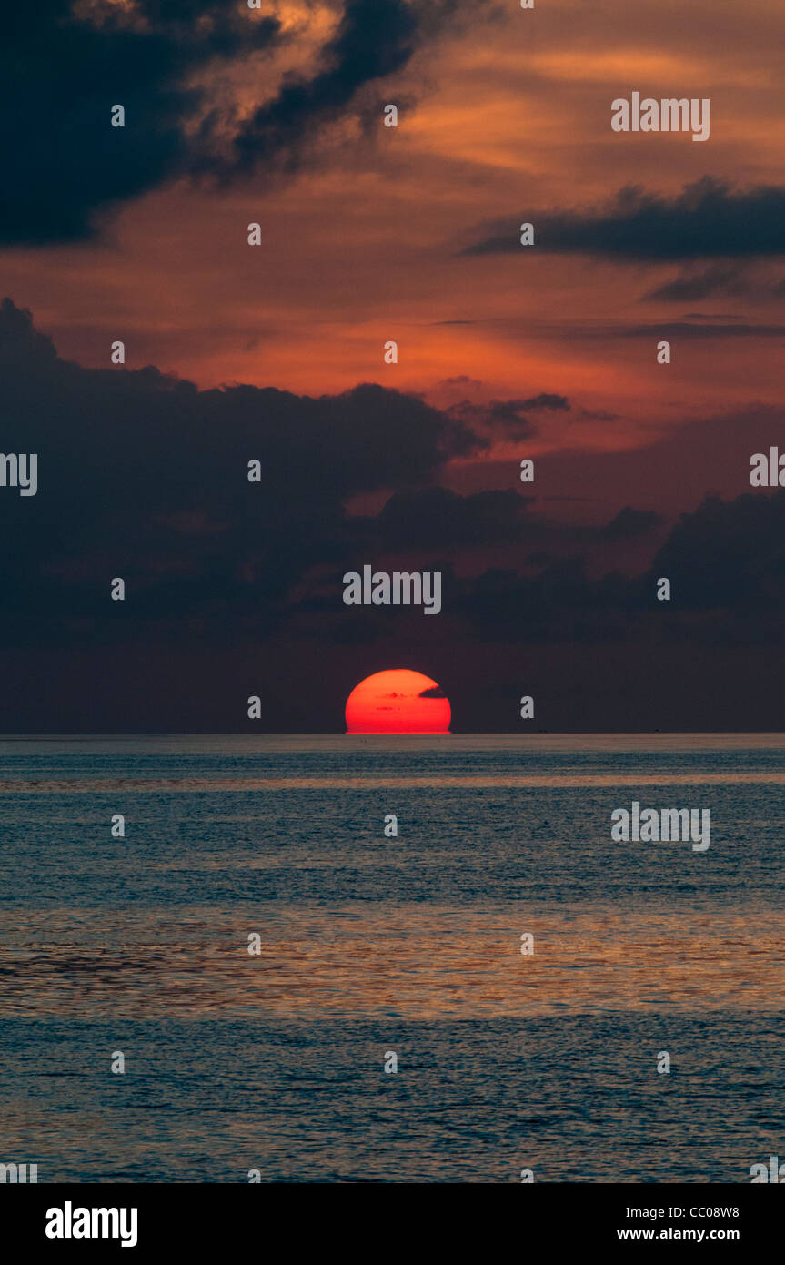The sun is partly below the horizon, with the calm waters of the Pacific Ocean in the bottom of frame and the orange clouds above. Taken at Swains Reef on the southern end of the Great Barrier Reef of the coast of Queensland, Australia. Stock Photo