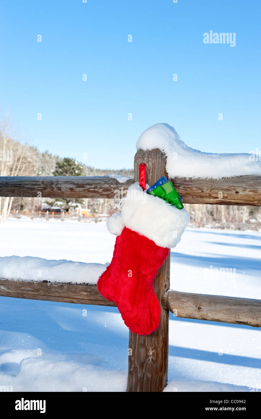 A Christmas stocking stuffed with presents hanging on a wooden fence in a wilderness resort mountain area. Stock Photo