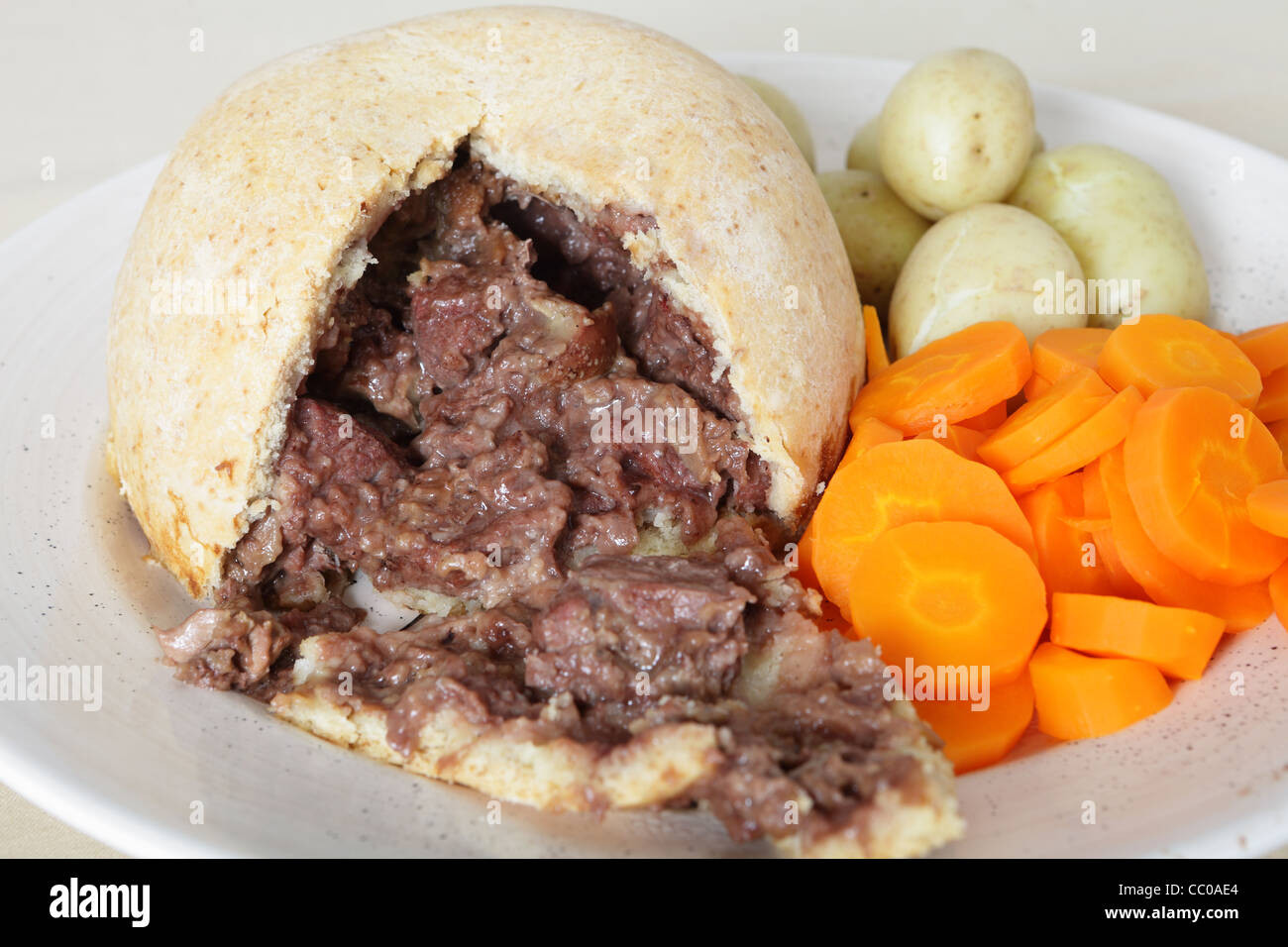 A serving plate with a steak and kidney suet pudding, boiled new