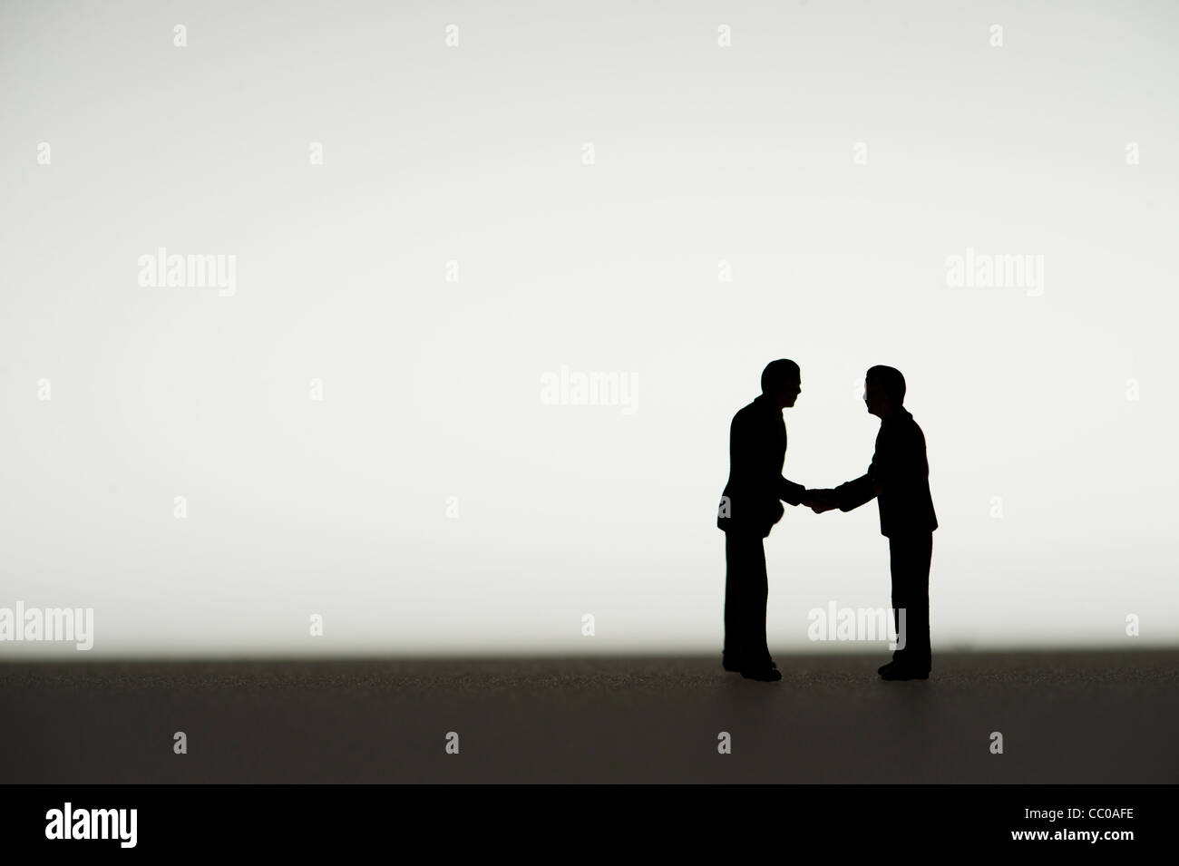 silhouetted small figures conceptual image for two business men meeting agreeing a deal shaking hands Stock Photo