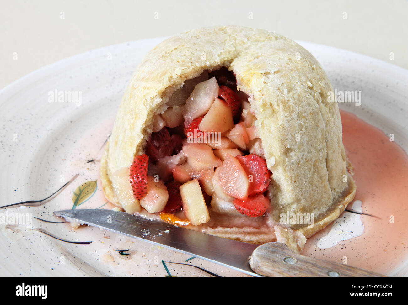 A traditional british steamed strawberry and pear fruit pudding on a serving dish, cut open, with the kitchen knife Stock Photo