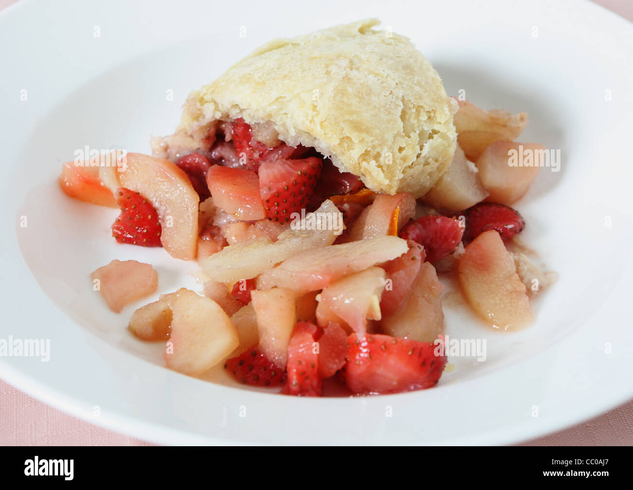 A portion of steamed pear and strawberry pudding in a suet pastry crust served in a white bowl Stock Photo