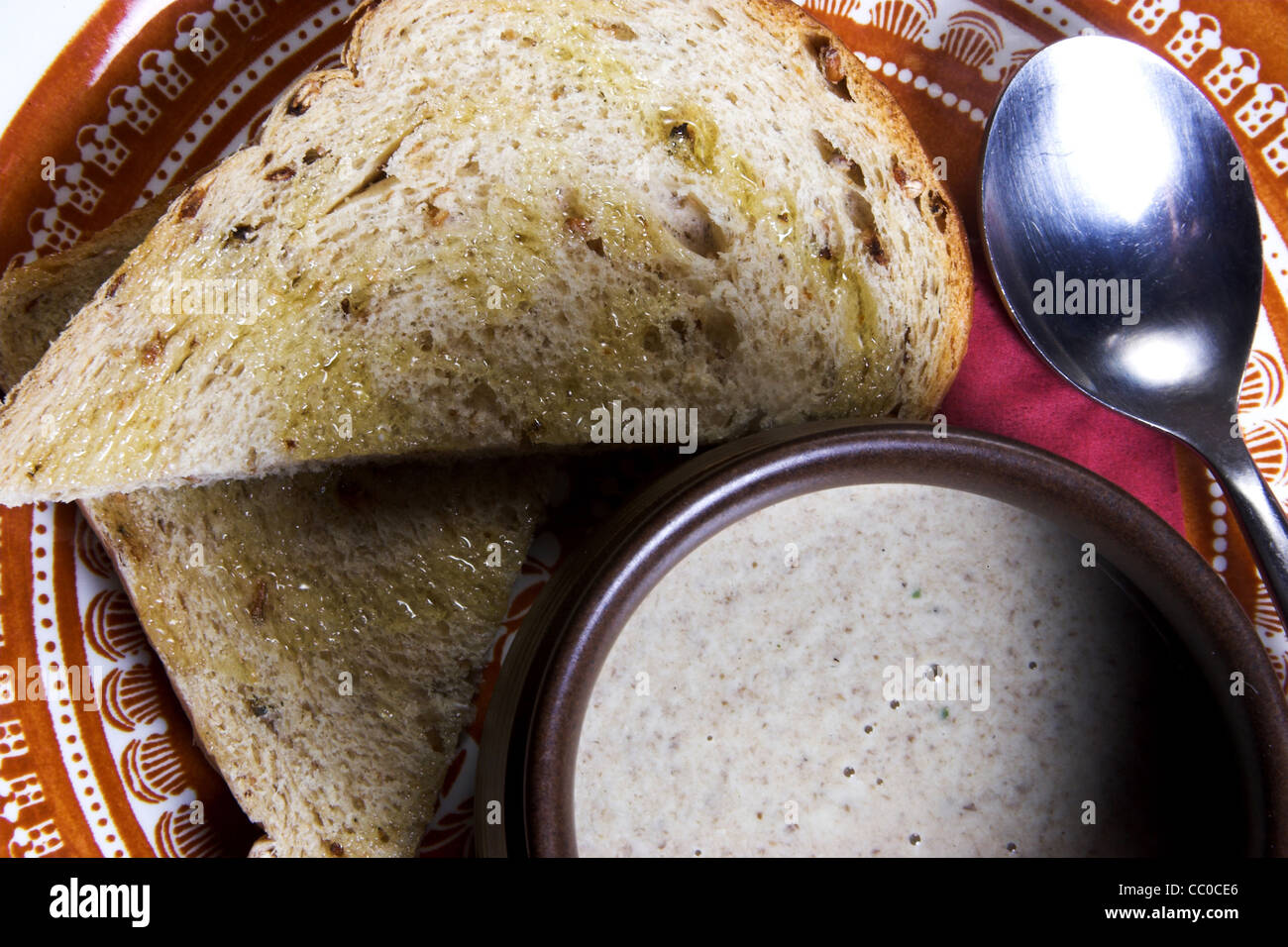 Bowl of mushroom soup with wholegrain slices of bread drissled in olive oil on a plate with a spoon. Stock Photo