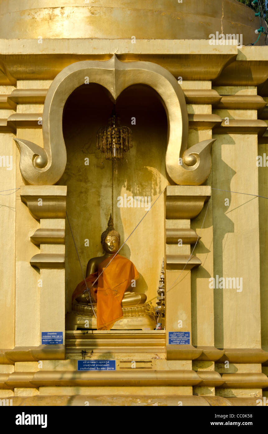 Gold Buddha statue with shawl draped on it in recess of stupa at a