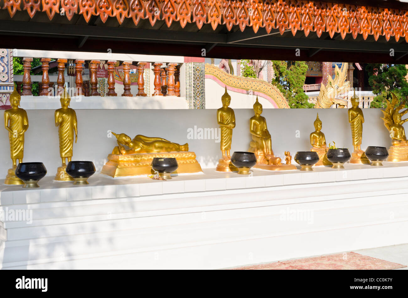 Several small gold Buddha statues on white mantle with black bowls in front at Buddhist temple in northern Thailand Stock Photo