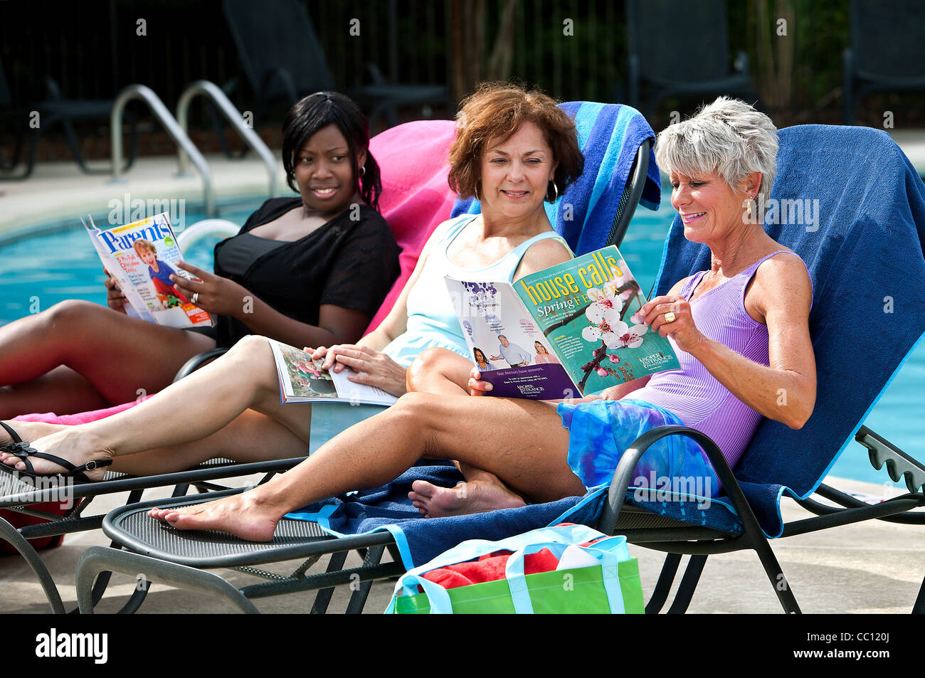 Three women enjoy themselves by the pool side. Stock Photo
