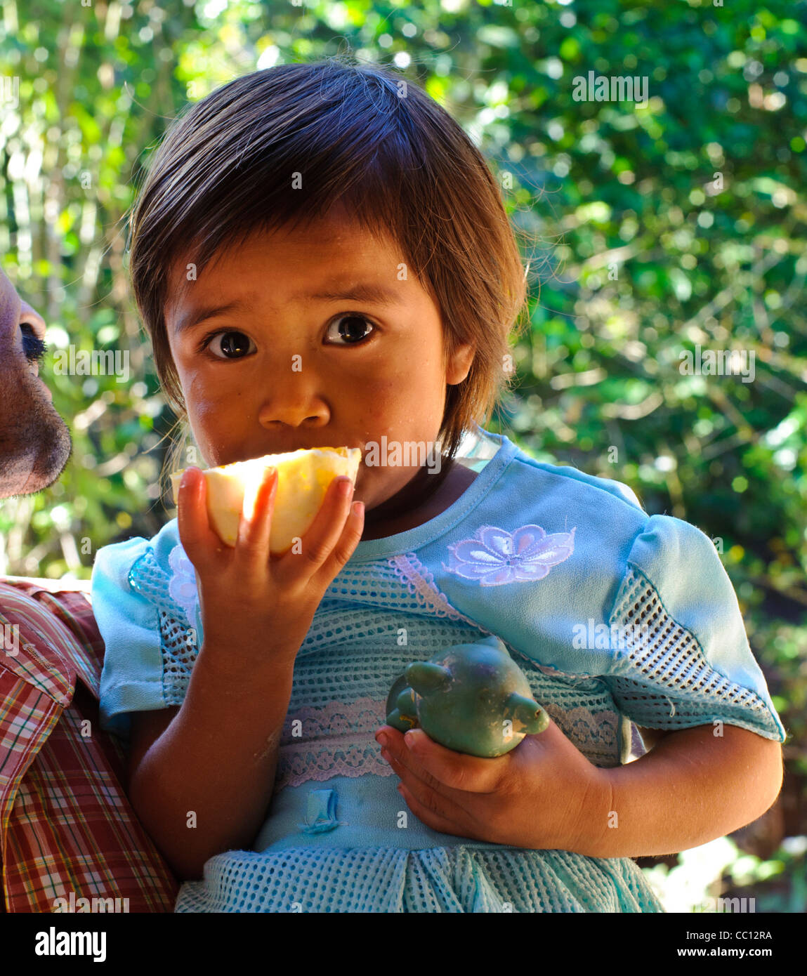 Young campesino girl eating an orange while her father holds her. Honduras Stock Photo