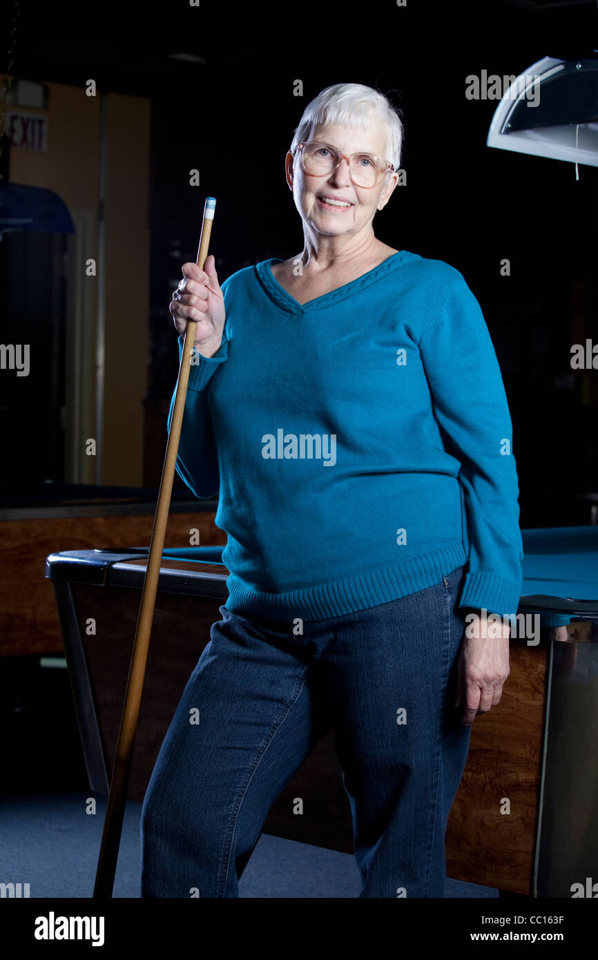 Senior citizen standing by a pool table holding a pool cue. Stock Photo
