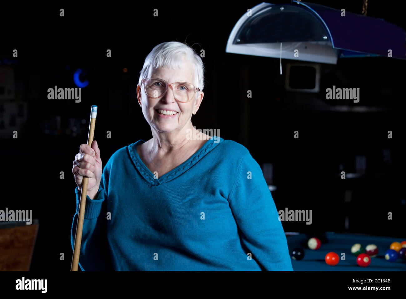 Senior citizen standing by a pool table holding a pool cue. Stock Photo