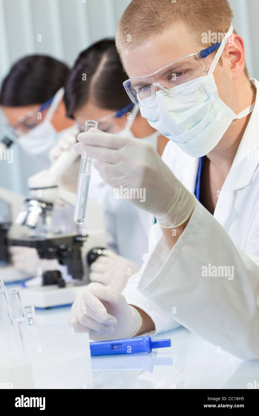 A male medical or scientific researcher or doctor looking at a test tube of clear liquid in a laboratory with microscopes Stock Photo