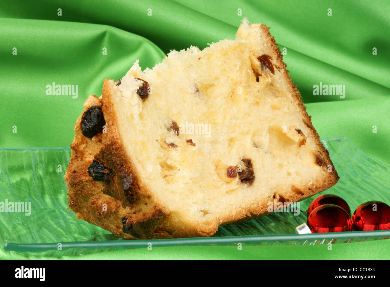 Panettone the italian Christmas fruit cake served on a transparent glass plate with some red glass ornaments. Stock Photo