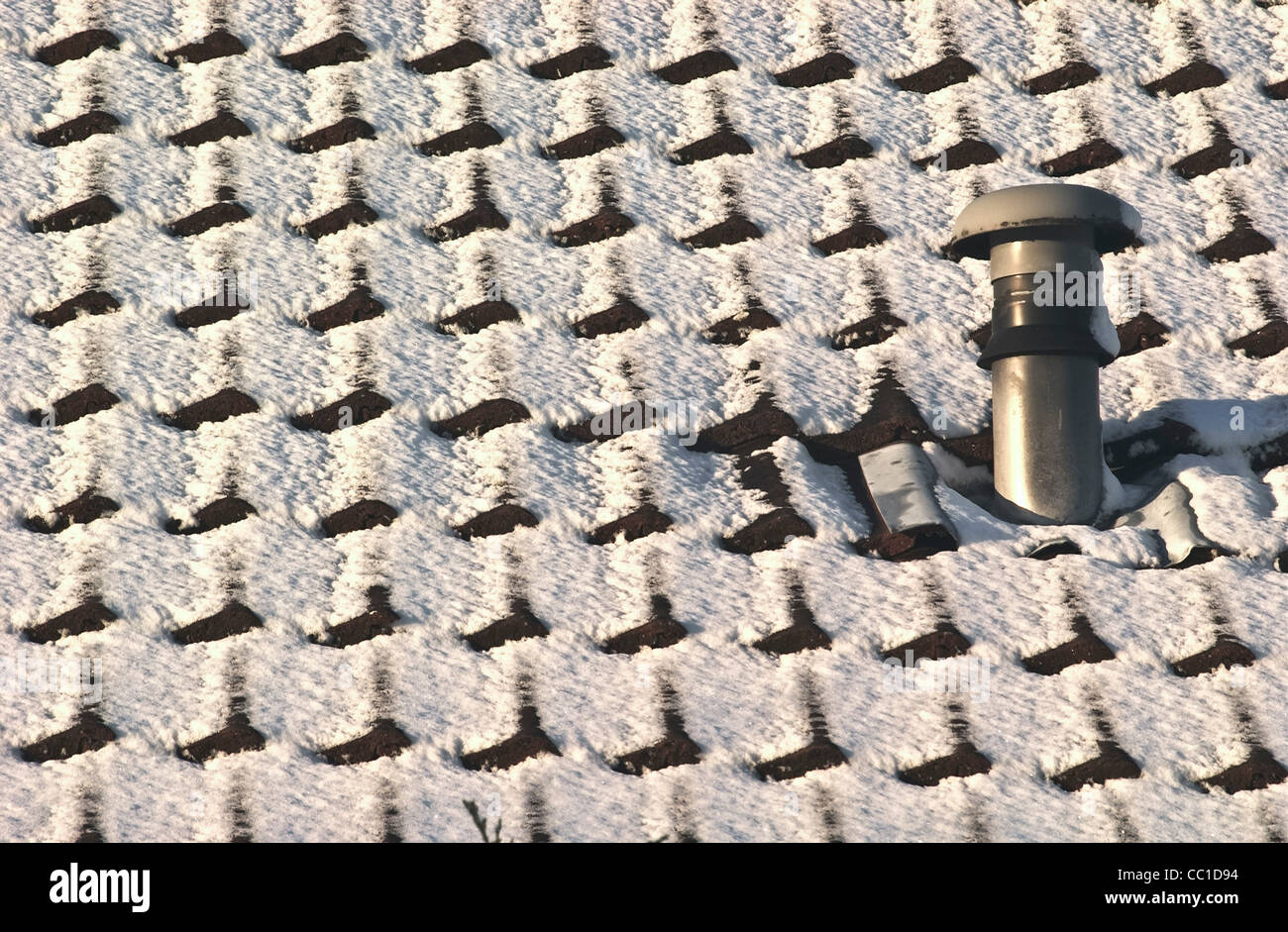 Snow covered tiled roof with central heating vent chimney Stock Photo