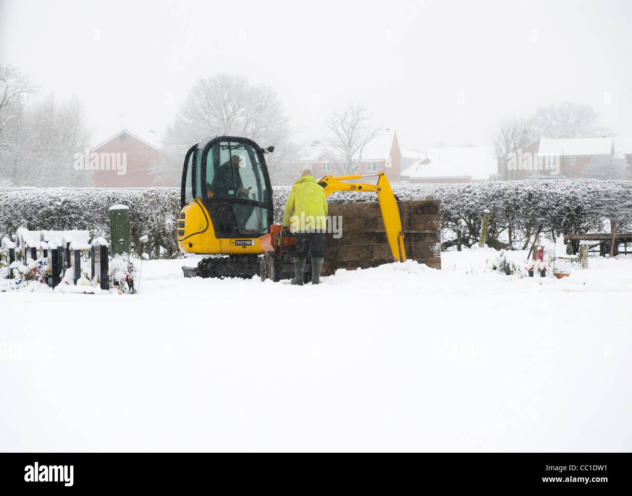 Gravediggers mechanically digging a grave with a small excavator in UK
