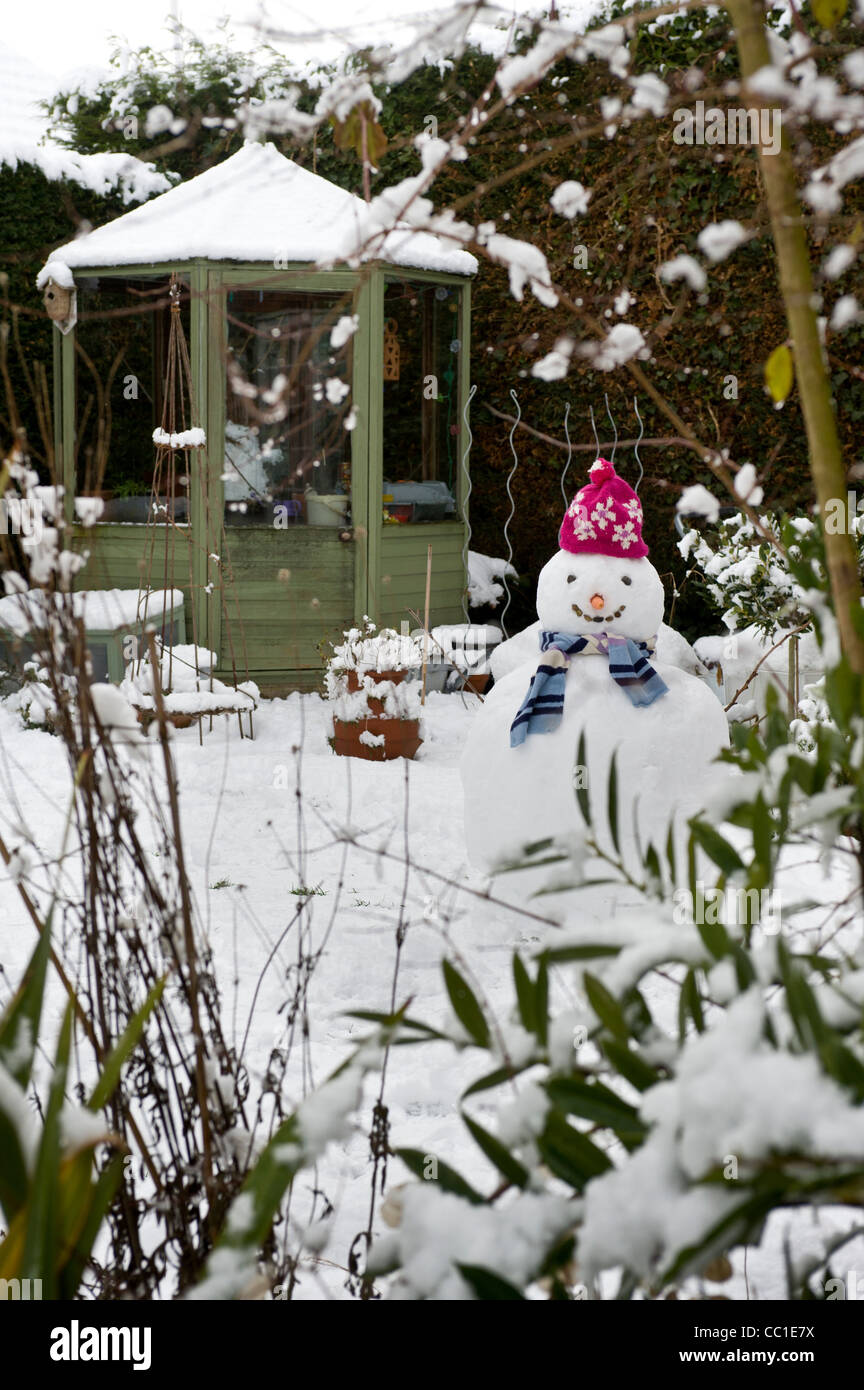Snow covered greenhouse with snowman in the foreground of a UK garden in winter. Stock Photo
