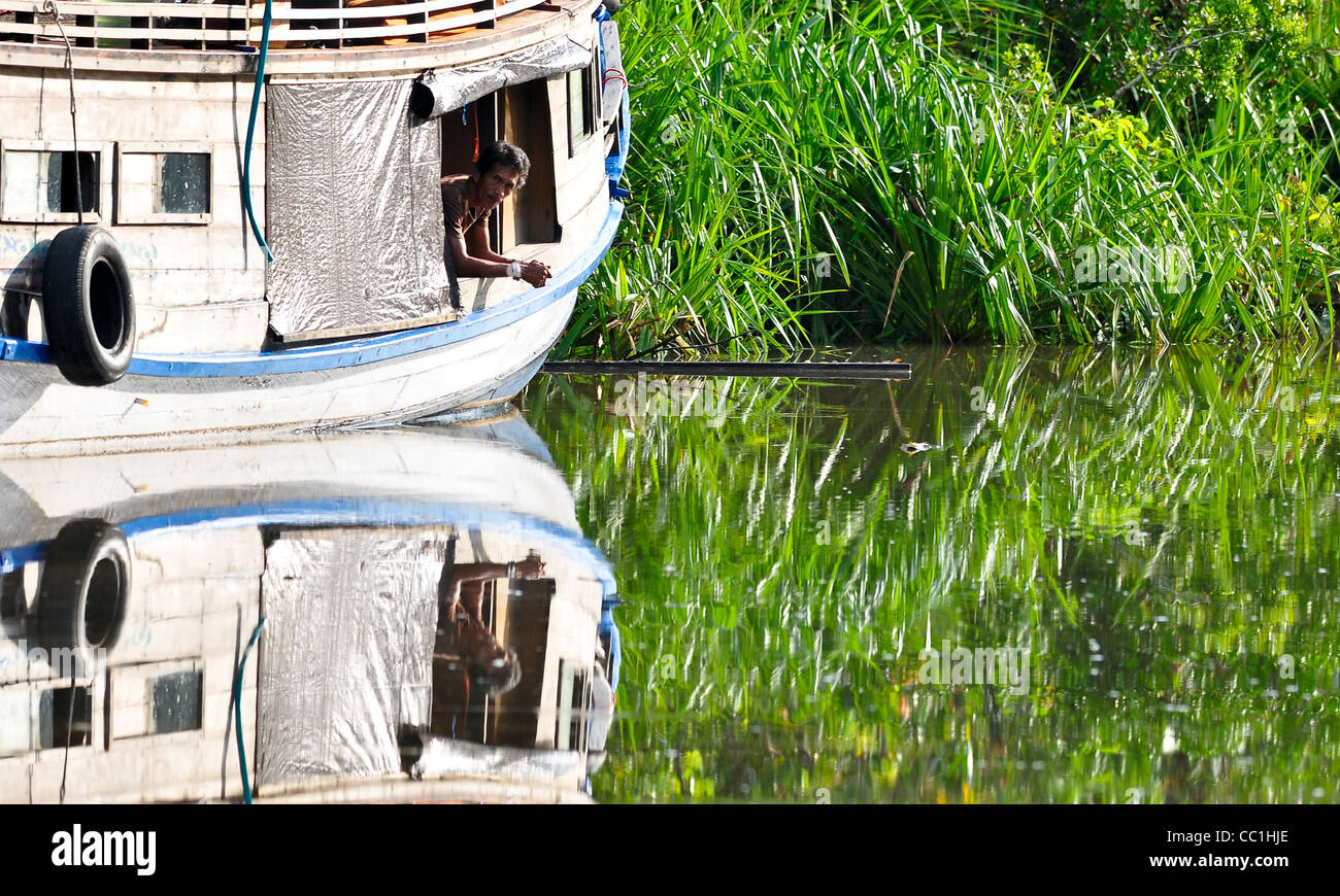 A riverboat (Klotok) crew member leans out of his boat on the Sekonyer River, Tanjung Puting NP, Borneo. Stock Photo