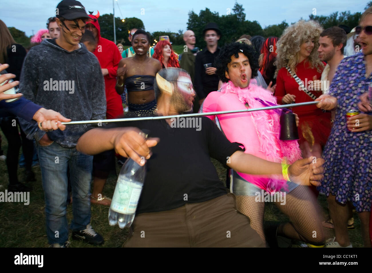 Two men in costume limbo dance beneath a pole at the Standon Music  Festival, Hertfordshire, UK Stock Photo - Alamy