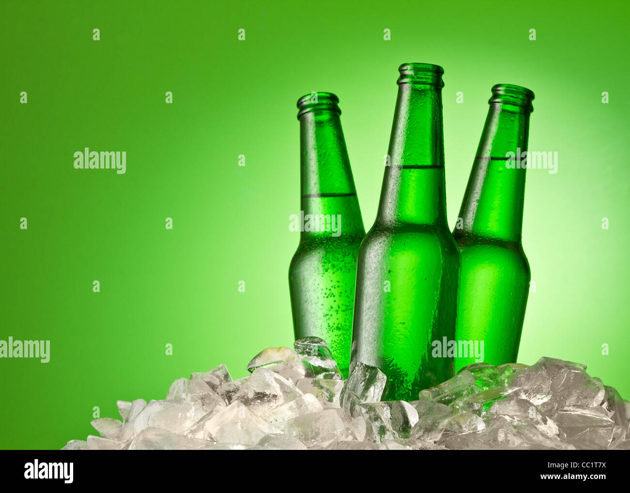 Three beer bottles getting cool in ice cubes. Isolated on a green. Stock Photo