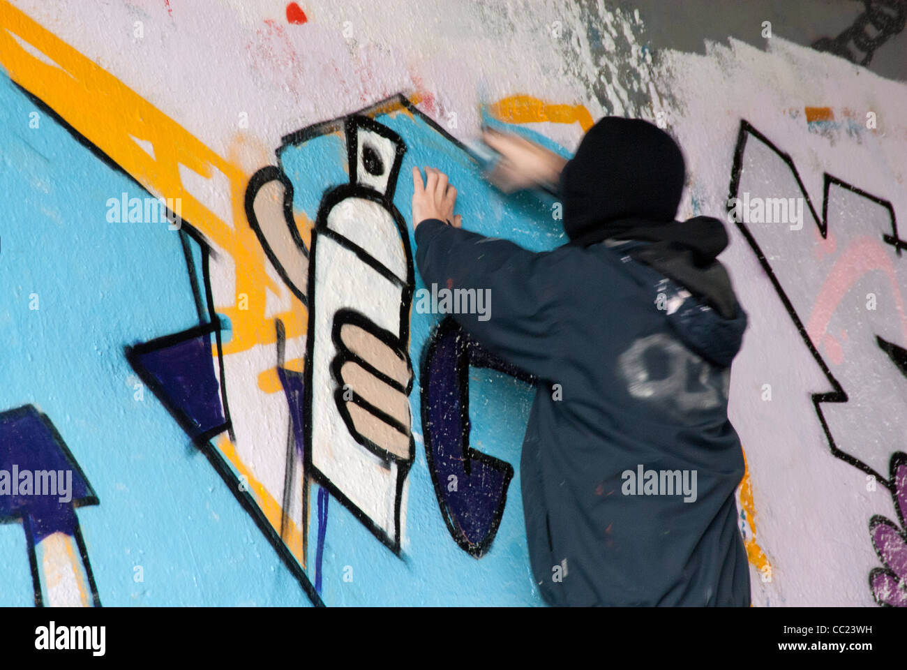 Tagging - Hooded young man spray painting graffiti. Note: Parts of man in blurred motion. Note: Parts of man in blurred motion. Stock Photo