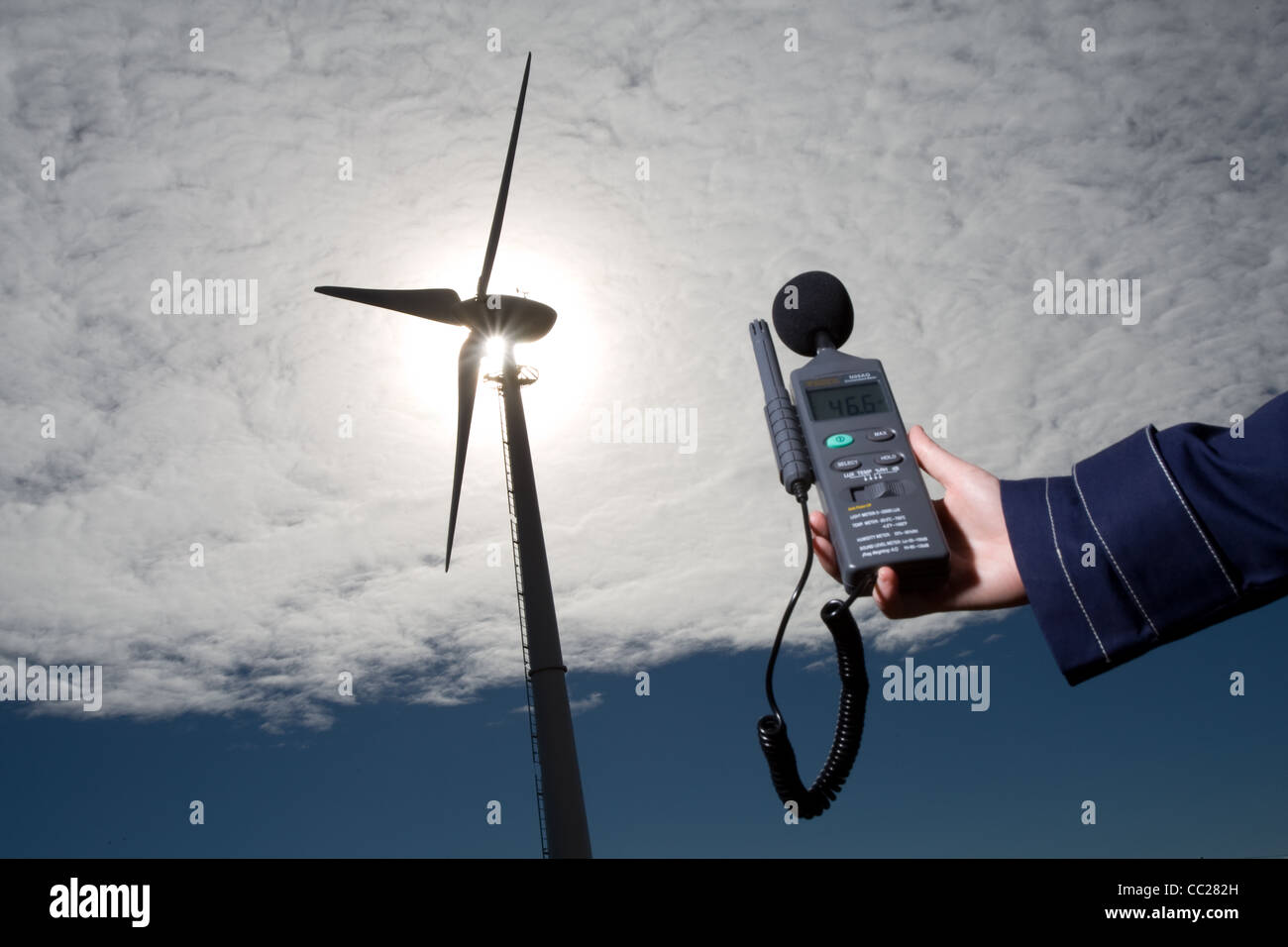 A sound level meter is held up to a wind turbine to measure the noise emitted in decibels. Stock Photo
